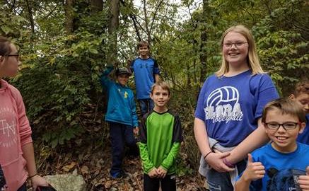 Teen REACH: Children in T-shirts, some smiling, stand in woods
