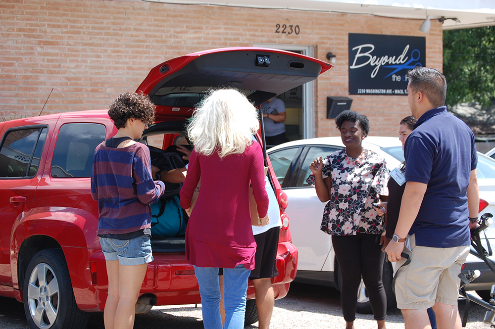 host homes: Group of people stand around opened trunk of minivan.