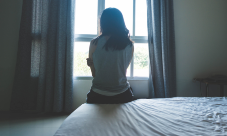 trafficking of girls: young, sad woman sitting on bed looking out window