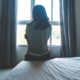 trafficking of girls: young, sad woman sitting on bed looking out window