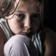 economic analysis of childhood exposure to crime/violence report; sad child on floor with black background looking down
