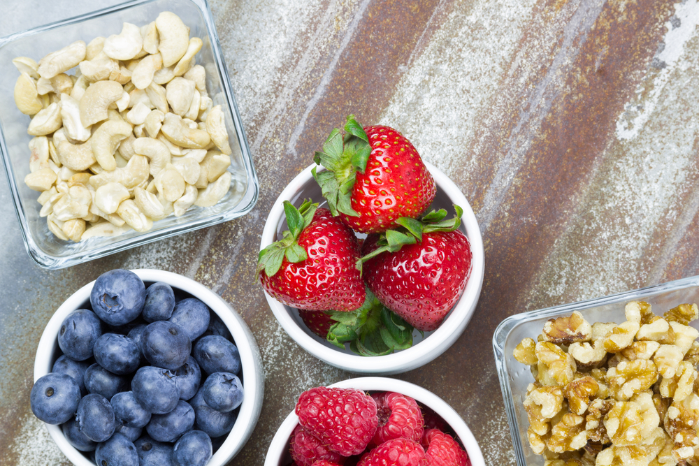 snacks: Healthy snack foods with small bowls of raspberries, blueberries, strawberries, cashews and walnuts 