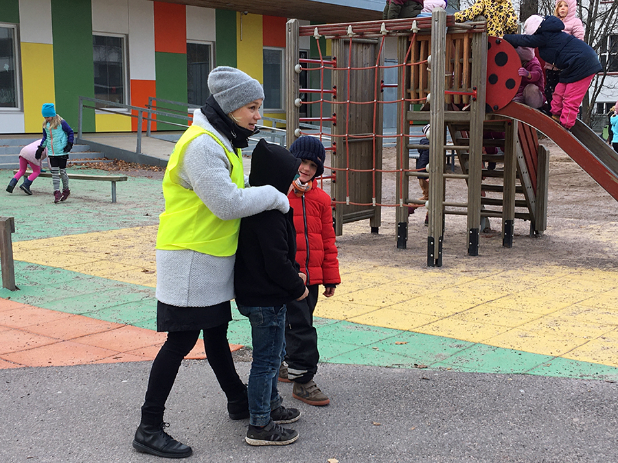 Finland: Warmly dressed woman puts arm around one of several children on playground