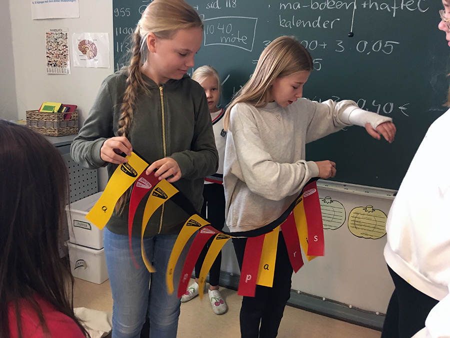 Finland: 2 blonde girls hold connected yellow and red ribbons in classroom
