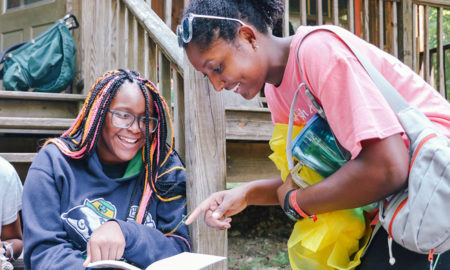 after-school: 2 smiling women look at book outdoors