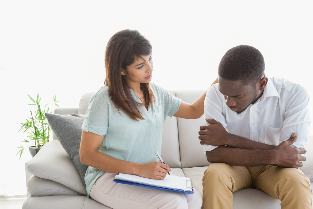 suicide: Therapist reassuring her upset patient, a young man of color, at therapy session