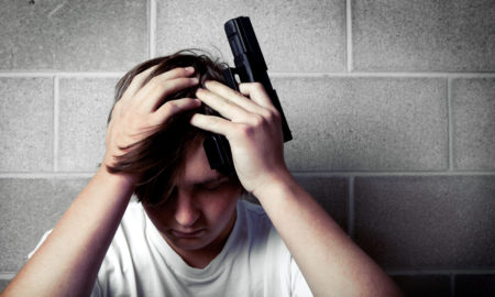 gun safety: Male teen with hands on head holding handgun