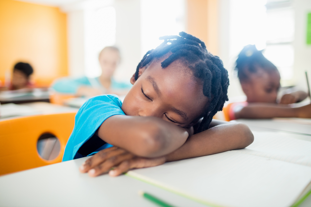 homeless: Child of color falling asleep at school desk.
