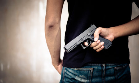 protection orders: Man in black T-shirt hiding gun behind his back.