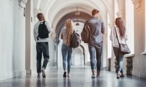 college campus well-being grants; four college students walking down campus hallway away from camera