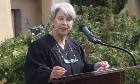 Carlsbad: Woman with short gray hair in black robe speaks at lectern.