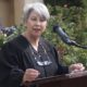 Carlsbad: Woman with short gray hair in black robe speaks at lectern.