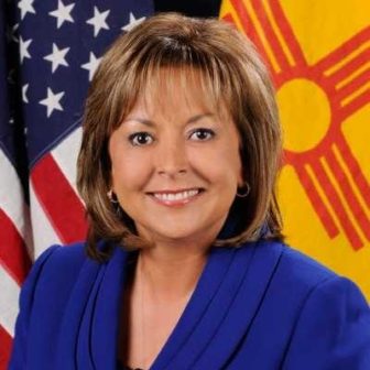 New Mexico: Smiling woman in blue suit in front of flags