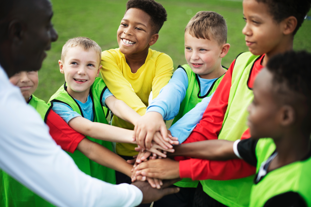coaching: Smiling junior football team stacking hands before a match with their coach