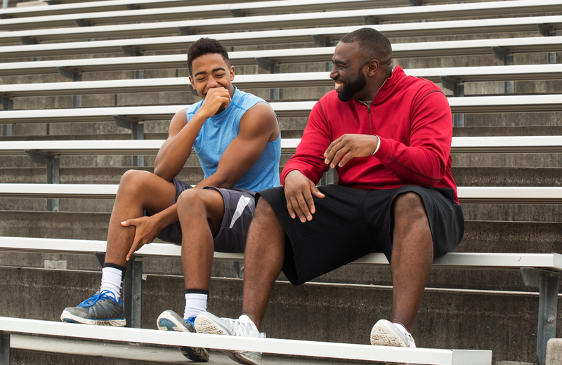 Youth mentoring, community-based mentoring program report: black teen male and mentor talking and laughing on bleachers