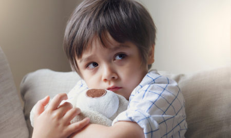 foster care: little boy sitting on sofa and cuddling teddy bear with scared face