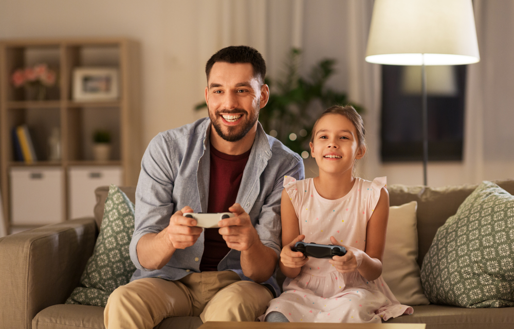 relationships: happy man and little girl with gamepads playing video game at home