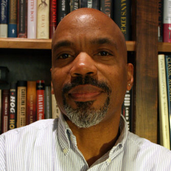 black boys: Man wearing button-down shirt with folded arms in front of bookcase