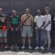 black boys: 6 boys in T-shirts and jeans with smiling man in middle wearing polo shirt and shorts in front of memorial.