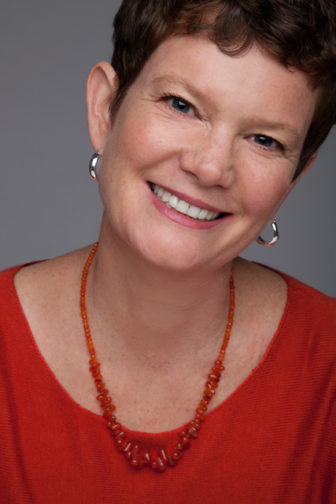 ost: Amy Lang (headshot), childhood sexuality, sexual abuse prevention expert, smiling woman with short brown hair, earrings, red top, red necklace