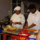 cooking: 2 women in white cooking uniforms work with food at steel counter