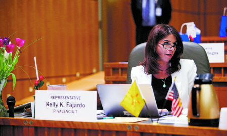 legislature: Woman in white blazer sits at large wooden desk with name card in front of her that says Rep. Kelly K. Fajardo R-Valencia-7