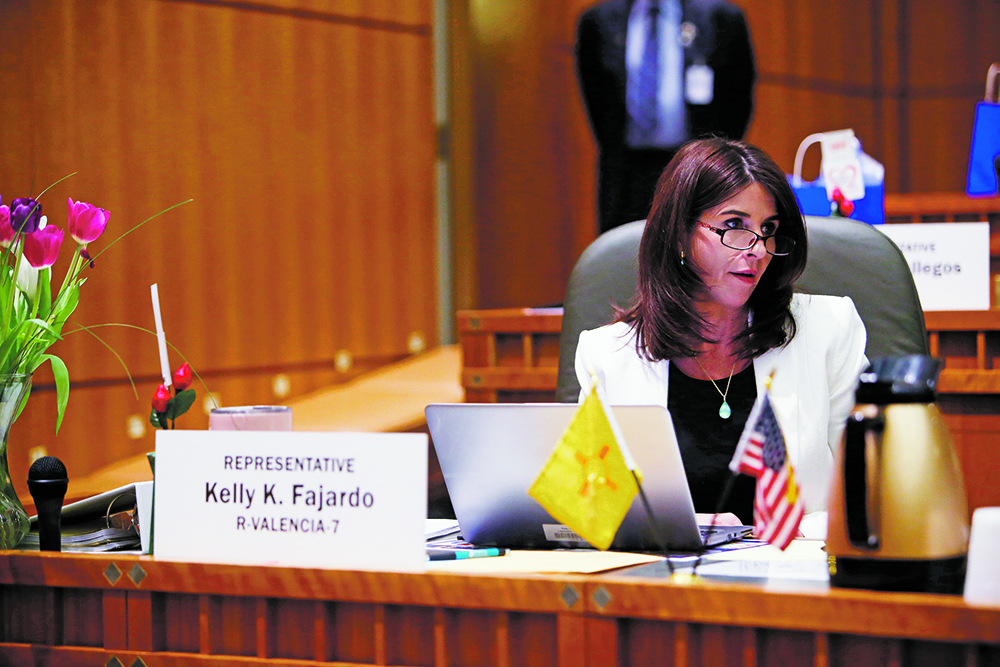 legislature: Woman in white blazer sits at large wooden desk with name card in front of her that says Rep. Kelly K. Fajardo R-Valencia-7