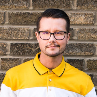 homeless: Alex Abramovich (headshot), scientist at Institute for Mental Health Policy Research, man with short dark hair, beard, mustache, wearing glasses, polo shirt, dark pants, leaning against brick wall outside 
