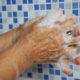 Soapy hands washing in front of blue & wite tiles wall.