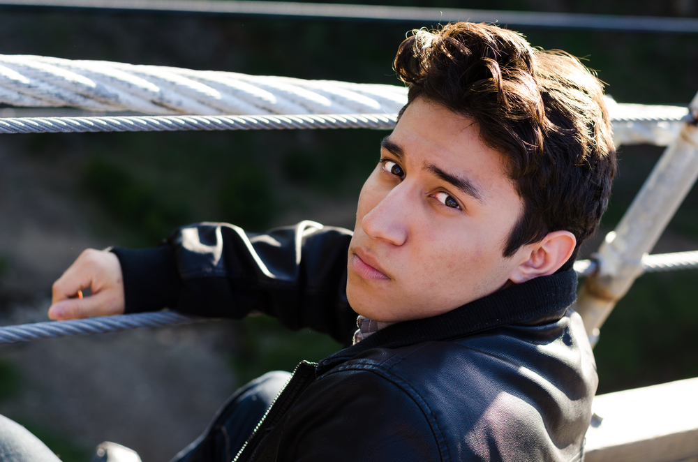 LGBTQ: sad-looking young man sitting on a suspension bridge, looking back at the camera