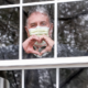 COVID-19 Community Healthcare and Education grants; man wearing medical mask in window making heart shape with hands