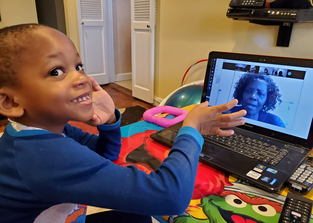remote learning: Smiling little boy gestures toward woman talking on laptop.