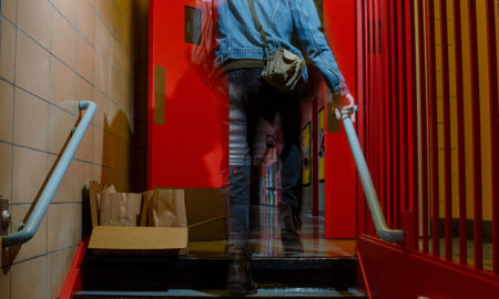 homeless: Person in jean jacket climbing stairs; tray of filled brown bags on landing