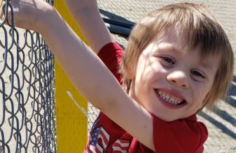 disabilities: Grinning little boy with light hair, red T-shirt, gray shorts, sneakers holding
