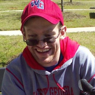 disabilities: Smiling man outside sitting on bench wearing ball cap, hoodie that says West Georgia Wolves