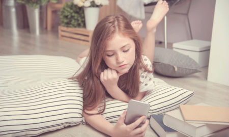 COVID-19: Little girl on FaceTime on phone lying on cushion on floor