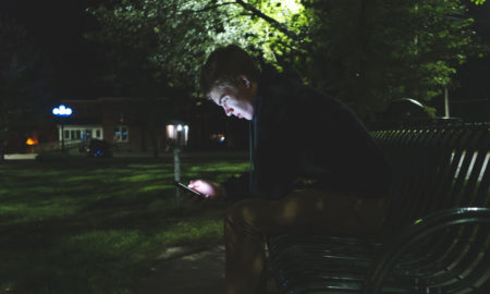 homeless: Depressed teenager on his cellphone while sitting on a park bench at night.