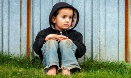 Birmingham region COVID basic needs grants; young worried child sitting in front of metal fence in hoodie