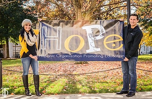Man and woman outside hold up banner that say hope hispanic organization promoting education