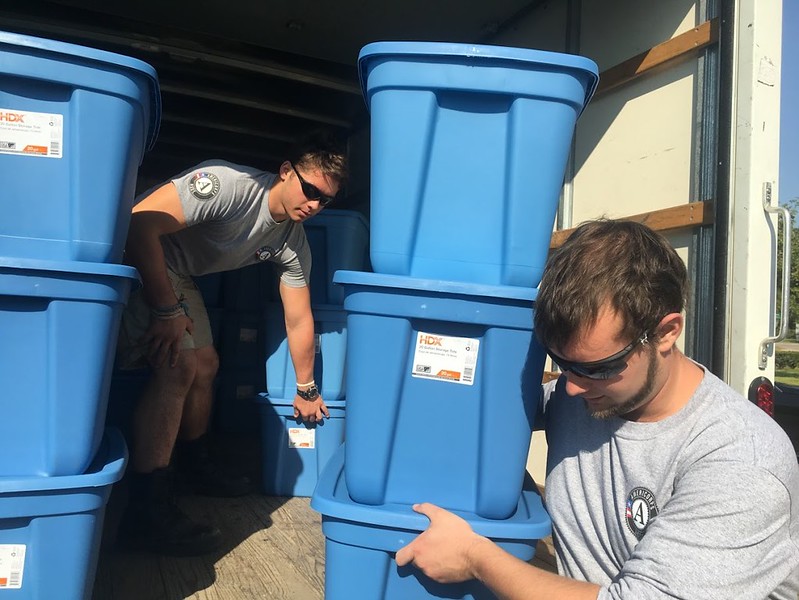 jobs programs: 2 young men pick up big blue rubber containers from truck