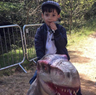 autism: Child in jacket sitting on plastic dinosaur outside