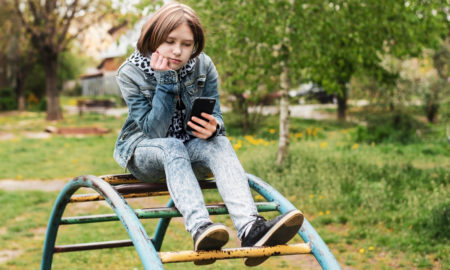 homelessness: Teenage girl sits on horizontal bar and looks at phone
