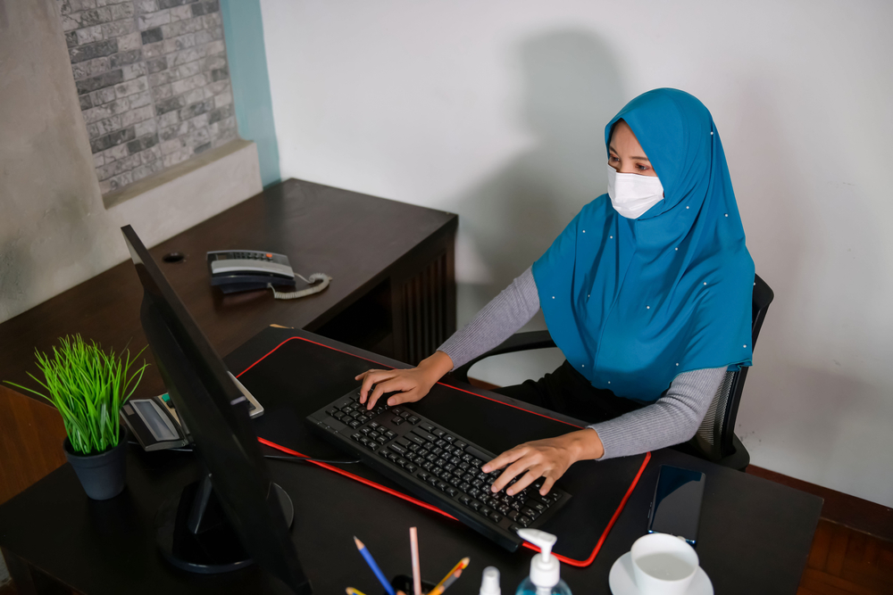 disability: Muslim woman in blue hijab, medical mask works on computer