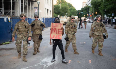 George Floyd: Man carrying sign reading let me live stands among men in military outfits