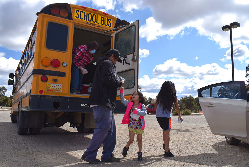 Gallup: 2 kids, adult carrying things walk from schoolbus to car.