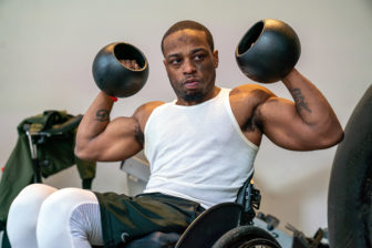 disabilities: Man with very short black hair in weights, workout outfit holding up weights