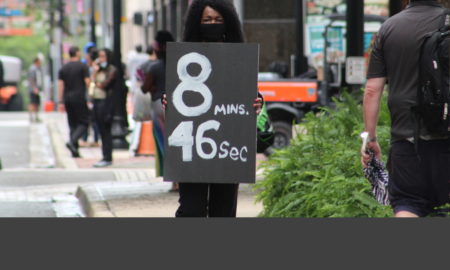 Jacksonville: Woman wearing mask holds a sign with 8 minutes 46 seconds on it