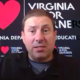 Virginia: Man with short brown hair in dark shirt speaks in front of black background labelled Virginia with pink hearts