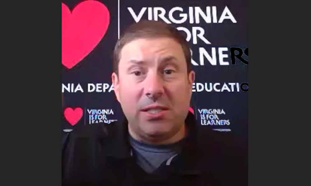 Virginia: Man with short brown hair in dark shirt speaks in front of black background labelled Virginia with pink hearts 