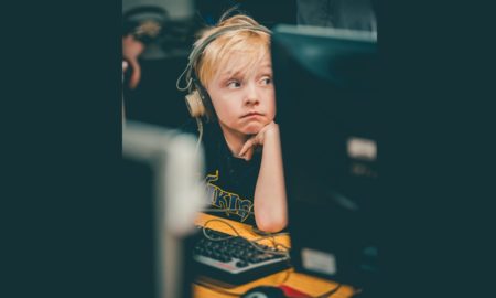 remote: Unhappy blond child wearing headphones looks away from computer